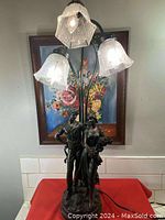 Full view of the vintage figurines table lamp with three glass shades illuminated.