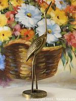 Front-facing view of the vintage solid brass crane figurine with detailed wing engravings and round base in front of a floral background.