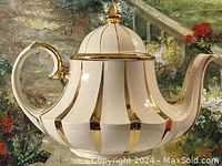 Side angle view of the white porcelain teapot with vertical fluted gold-trimmed panels and gold-trimmed handle and spout.