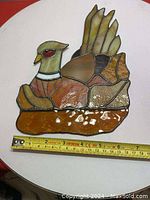 Stained glass bird panel lying flat with measuring tape showing approximately 7 inches wide