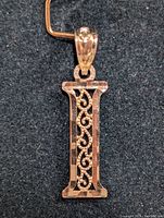 Close-up photo of the 10K gold pendant laid on dark fabric, showing front view with intricate filigree work.