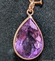 Close-up photo of 10K gold pendant with faceted purple pear-shaped amethyst gemstone placed on black fabric.