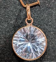 Close-up front view of round blue topaz pendant set in 10K gold bezel with attached bail.
