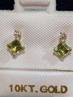 Front view of the 10K gold earrings featuring square peridot stones and round diamonds, displayed in original box with 10KT GOLD label.