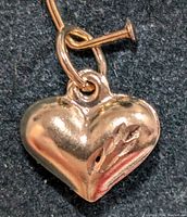 Close-up image of the small 14K gold heart pendant showing its polished surface, rounded shape, and small attachment loop.