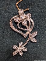 Close-up view of 14K gold pendant with floral heart design and cubic zirconia stones on petals and leaves.