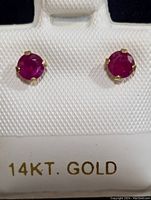 Front view of the two 14K gold ruby stud earrings set on a white display card marked 14KT GOLD.