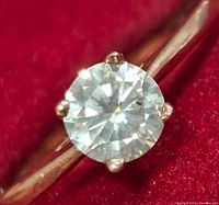Close-up top view of round brilliant diamond showing prong setting on red background
