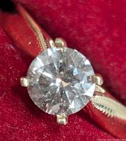 Close-up top view of round brilliant diamond in four-claw setting on red background