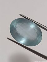 Close-up photo of aquamarine gemstone held by jeweler tweezers showing facets and clarity.