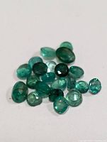 Multiple genuine emerald gemstones with varied cuts and green tones shown against a plain white background.
