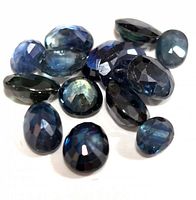 Group of 13 faceted blue sapphire gemstones in various cuts and shapes, showing light to dark blue hues and reflective facets.
