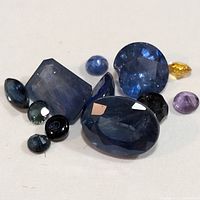 Photo showing mixed shapes and colors of loose sapphire gemstones including deep blue, light blue, yellow and purple stones.
