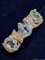 Close-up front view of silver ring showing pear-shaped blue topaz center flanked by oval and round blue topaz stones with clear accent stones on silver band.