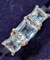 Close-up view of ring showing three square-cut blue topaz stones in a row set in silver prongs.