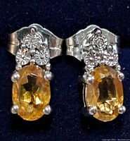 Close-up front view of both silver stud earrings showing oval faceted citrine stones and decorative small diamond accents