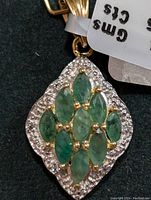 Close-up front view of silver pendant showing emerald cluster and surrounding diamond-like stones