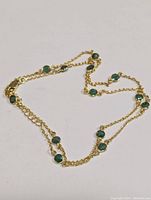 Full view of silver chain necklace with multiple round green stones spaced along the chain.