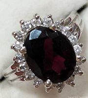 Close-up front view of the silver ring with oval garnet and halo of cubic zirconia stones showing details of the stones and prong settings.