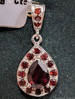 Close-up photo showing the front face of a silver pendant with a large pear-shaped garnet and smaller round garnets surrounding it on the pendant body and bail.