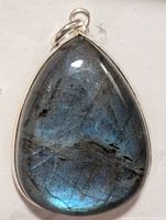 Close-up photo of a teardrop-shaped labradorite pendant with silver setting showing blue iridescent reflections and natural stone markings.