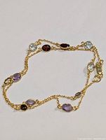 Photo showing full necklace laid flat with visible multi-colored oval and round gemstones and lobster clasp