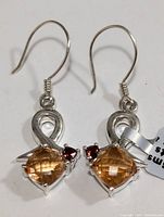 Pair of silver hook earrings with cushion-cut orange mystic quartz and small red garnet gemstones set in a looped silver design.