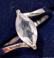 Close-up of silver ring with marquise rose quartz gemstone against a dark blue background. The rose quartz stone is clear pale pink and faceted.