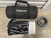 Photo of the Aputure branded black carrying case, folded softbox dome, and circular mount ring laid out on a floor.