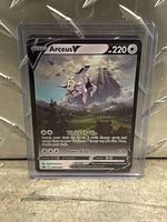 Front view of Arceus V Pokemon card in protective sleeve showing artwork, stats, and moves.