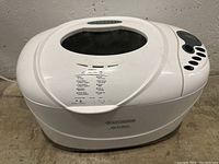 Front and top angle view of the Black+Decker white bread maker with control panel and viewing window.