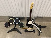 Video game controllers including a Rock Band drum kit with four colored pads, foot pedal, and black plastic stands with a black and white guitar controller.
