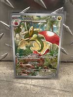 Holographic Flapple Surging Sparks Pokémon card in protective sleeve on metallic background. Shows card details and art clearly.