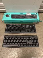 Two Logitech MK270 wired keyboards; one in original box and one out of box, lying on floor.