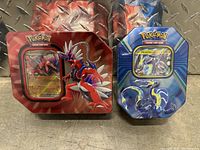 Two sealed Pokemon TCG tins, one featuring Miraidon EX and one featuring Koraidon EX, clearly showing promotional cards through packaging.