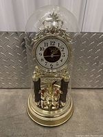 Full view of Seiko dome clock showing gold-tone base, ornate metal frame, white dial with black numerals and gold hands, clear glass dome, and rotating pendulum.