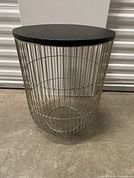 Side view of the round side table showing the metal wire basket base and black top.