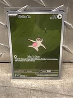 Close-up of Slakoth Pokémon trading card in a protective sleeve on a concrete surface.