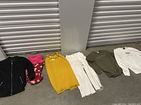 Seven women's clothing items laid on floor including jacket, pants, and tops