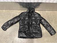 Full view of women's black puffer jacket laid flat showing long sleeves, quilted pattern, snap button and zipper closure.