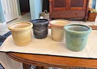 Four ceramic planters placed on a wooden surface, showing variety in colors and slight use marks.