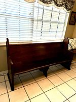 Full view of the antique wooden bench placed near a window showing its full length and structure.