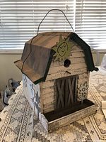 Side and front views of a barn-style wooden birdhouse with metal roof, distressed with rustic paint and painted enjoyably with sun and flower designs.