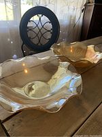 Photo showing two amber carnival glass serving bowls on wooden table with ruffled edges and iridescent finish