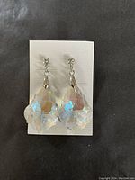 Pair of clear faceted crystal drop earrings on a white card, showing reflective prismatic colors and silver-tone hooks.