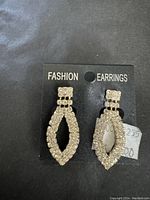Pair of elegant rhinestone fashion earrings on black card labeled 'Fashion Earrings'. Clear rhinestones form elongated teardrop shape with square cluster at top.