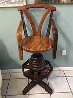 Front view of a heavy wooden stool showing the round seat, worn armrests, V-shaped backrest, and the octagonal base resembling an ox wheel.