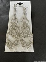 Photo showing pair of Lola dressy formal dangling earrings with intricate rhinestone design on the original packaging card stating Nickel & Lead Free.