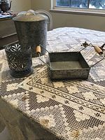 Photo of galvanized metal ice bucket, decorative candle holder, and square metal basket with wooden handles on a lace tablecloth.