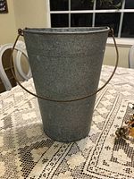 Gray galvanized metal bucket-shaped wall planter with round front and flat back for mounting, with rusty hanging handle.